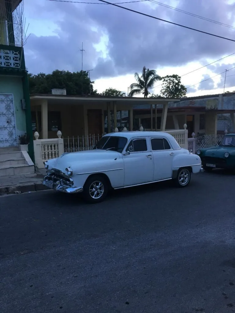 A photo of an old-school car outside a house in Cuba.